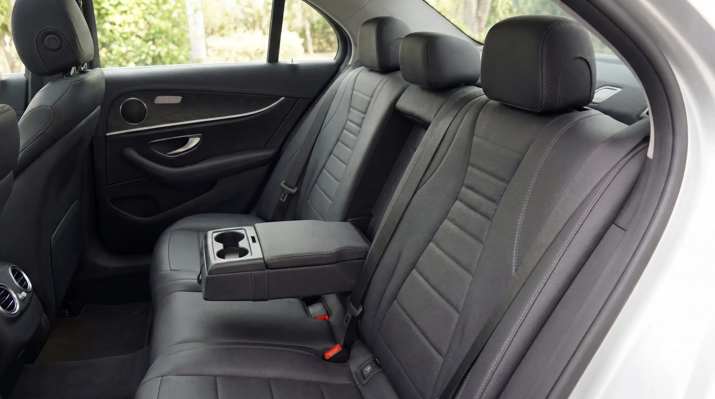 Mercedes-Benz E-Class rear seat detail — black leather with center armrest, soft daylit view through the windows