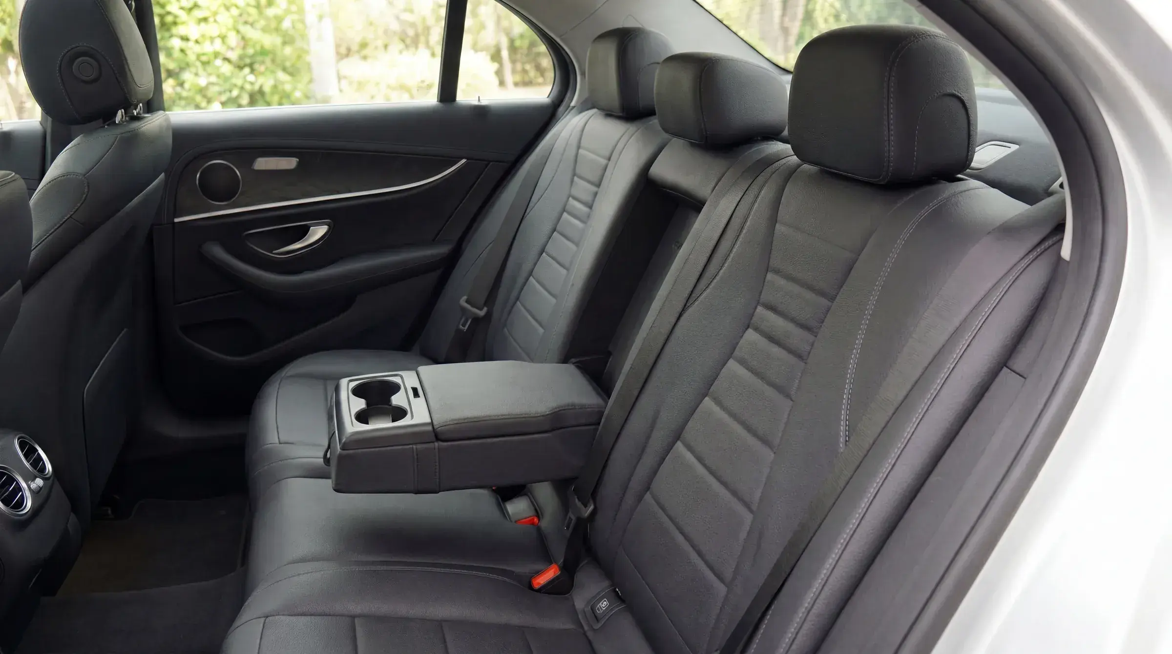 Mercedes-Benz E-Class rear seat detail — black leather with center armrest, soft daylit view through the windows