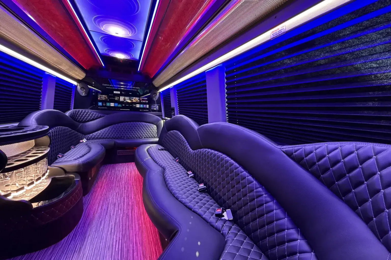 Limo Sprinter party cabin — wrap-around purple quilted-leather lounge seating with a bar, TV screen and purple ambient party lighting